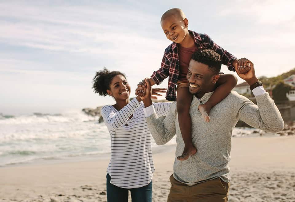 Family on beach with dad carrying young son on this shoulders
