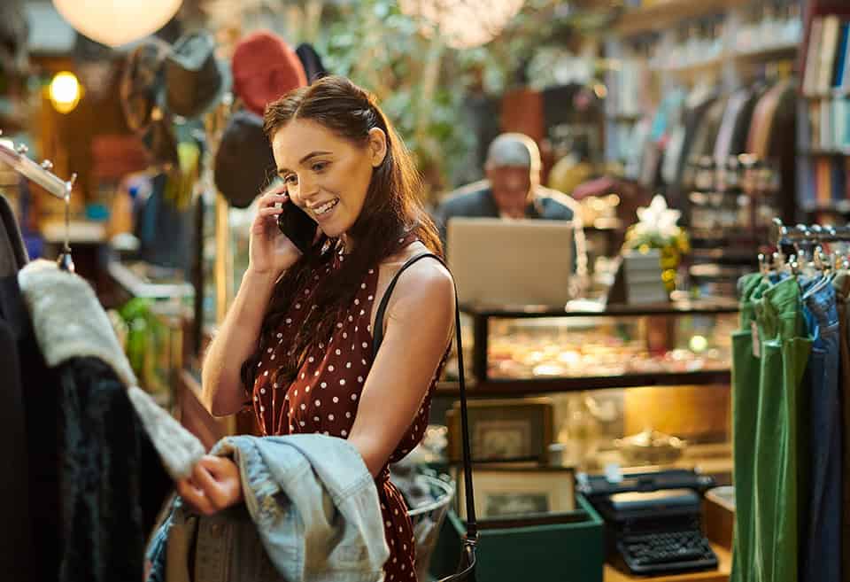 Person smiling and talking on the phone while browsing a vintage clothing store