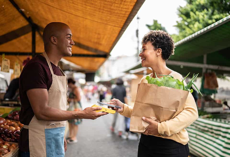 Vendor and shopper smiling while shopper is paying with their mobile wallet at the farmer's market