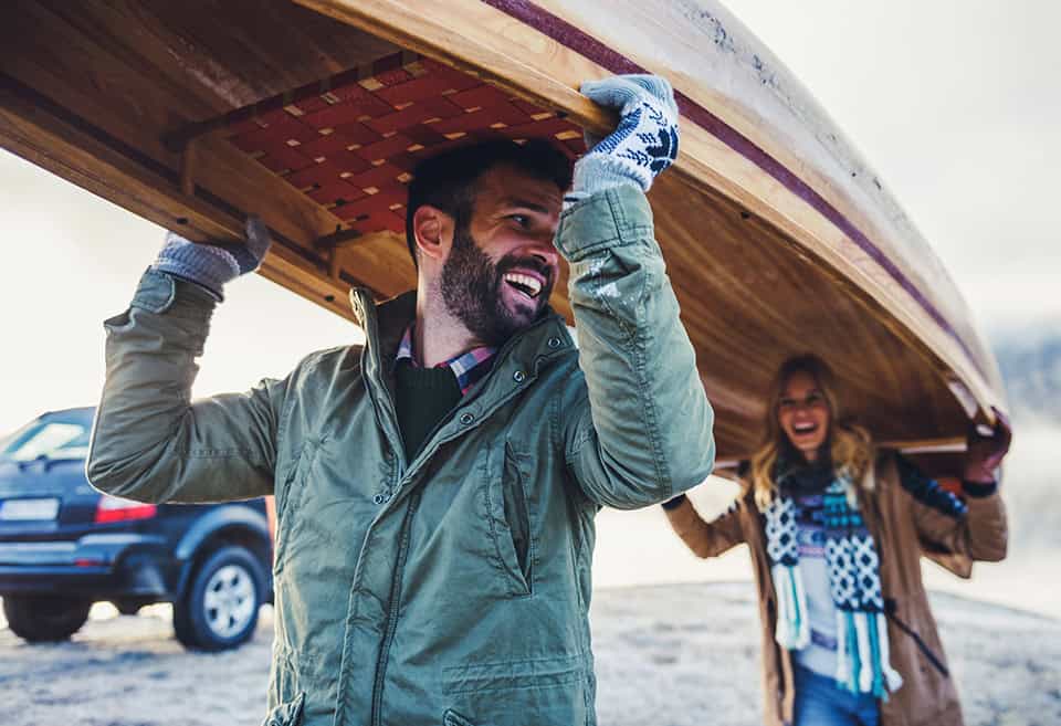 A couple smiling and laughing while carrying a canoe over their heads