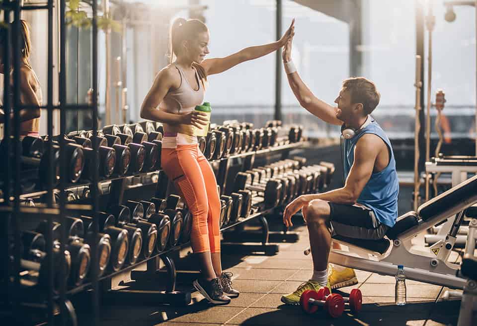 Two people dressed in athletic clothing high fiving in a gym after a workout