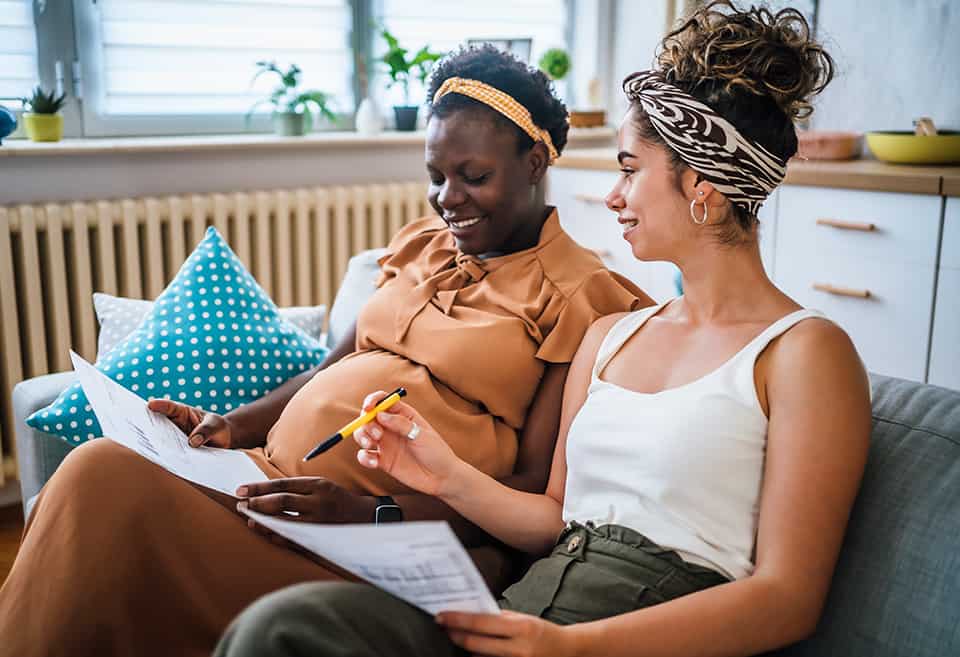 Pregnant couple sitting on couch paying bills