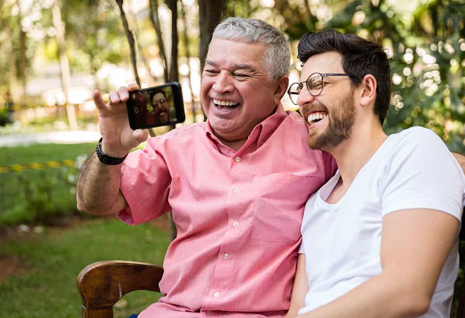 Two people smiling and laughing while sitting on a bench taking a selfie on a phone