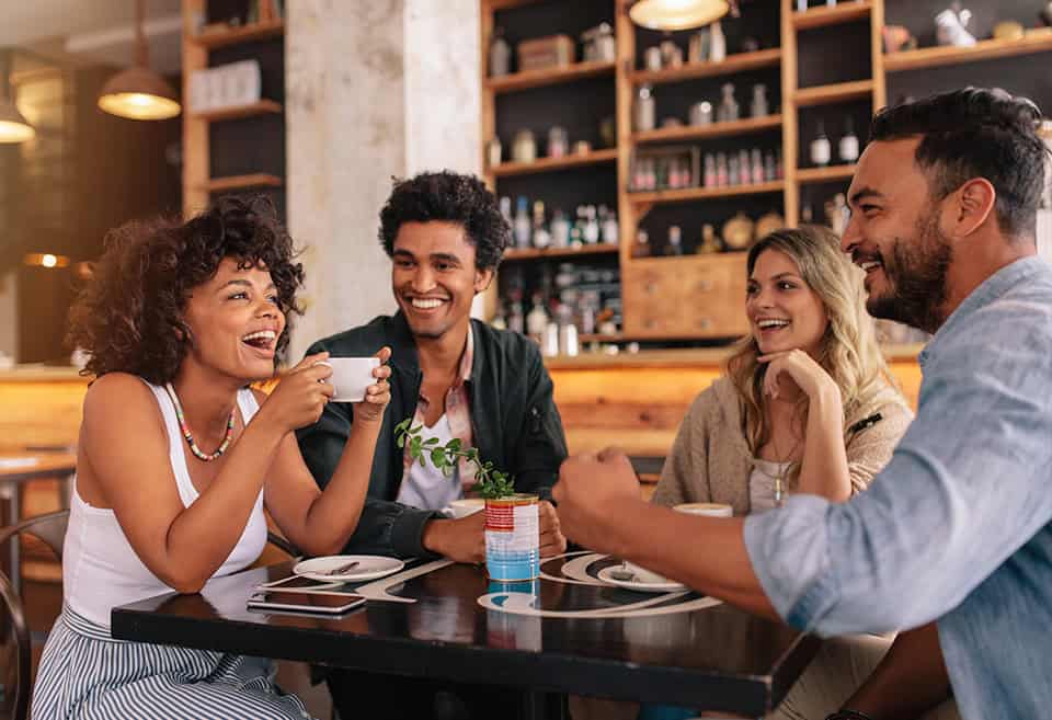 Group of friends laughing while sitting around a table at a coffee shop