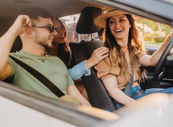 A group of three friends smiling and laughing in a car with the windows down