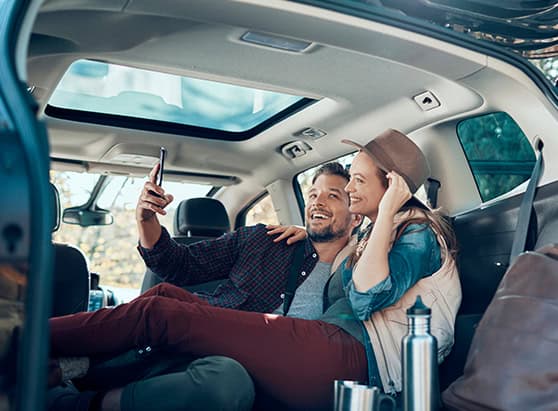 A couple smiling and taking a selfie as they lounge in the back of their car