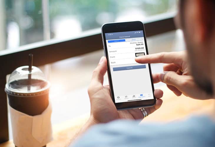 Man in coffee shop looking at mobile check deposit on his smartphone