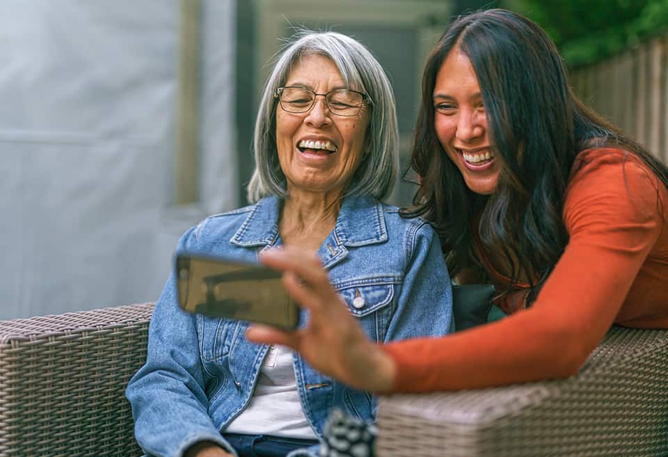 Mother and daughter laughing while looking at smartphone