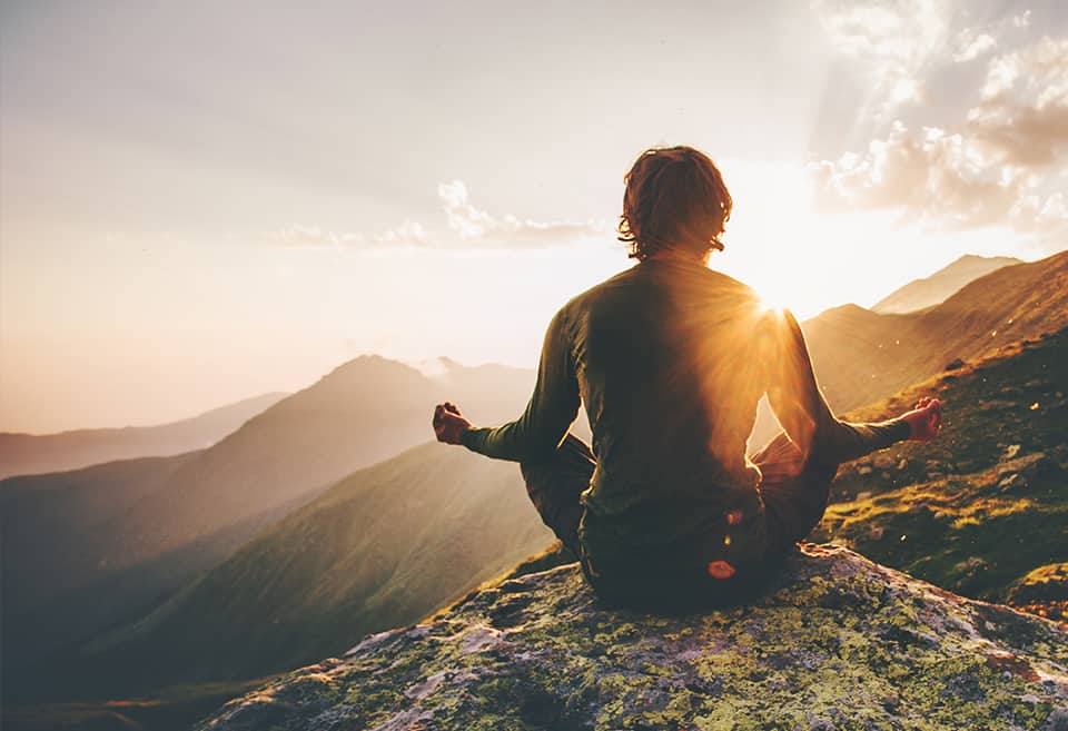 Person meditating on top of a mountain at sunset