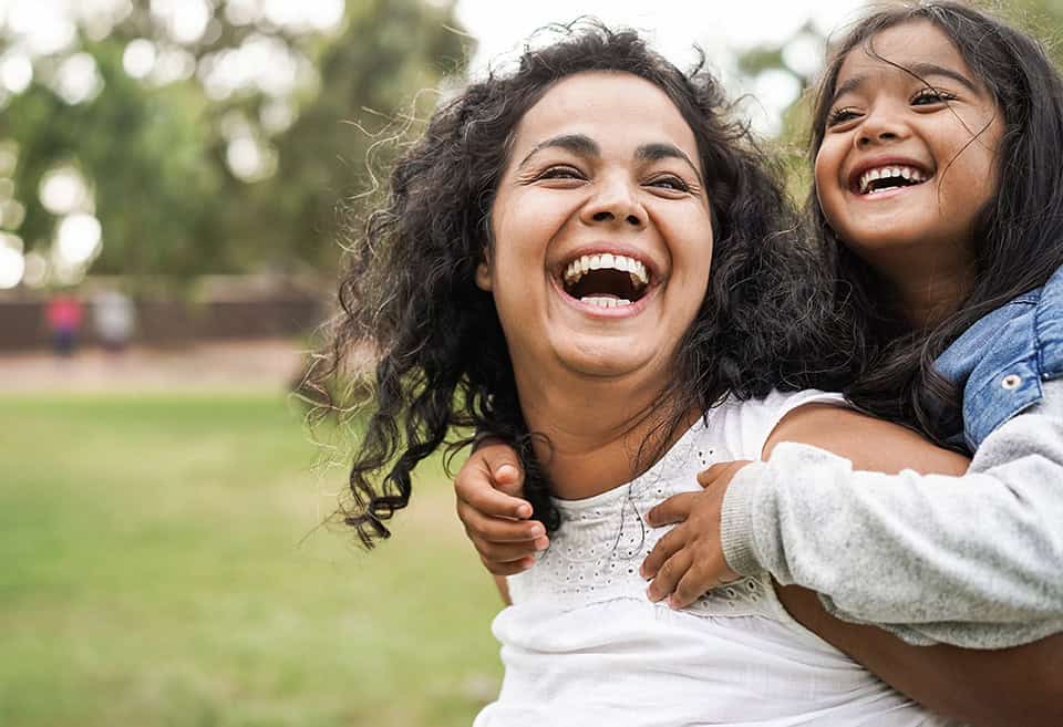 A parent smiling and laughing with their young child riding piggyback