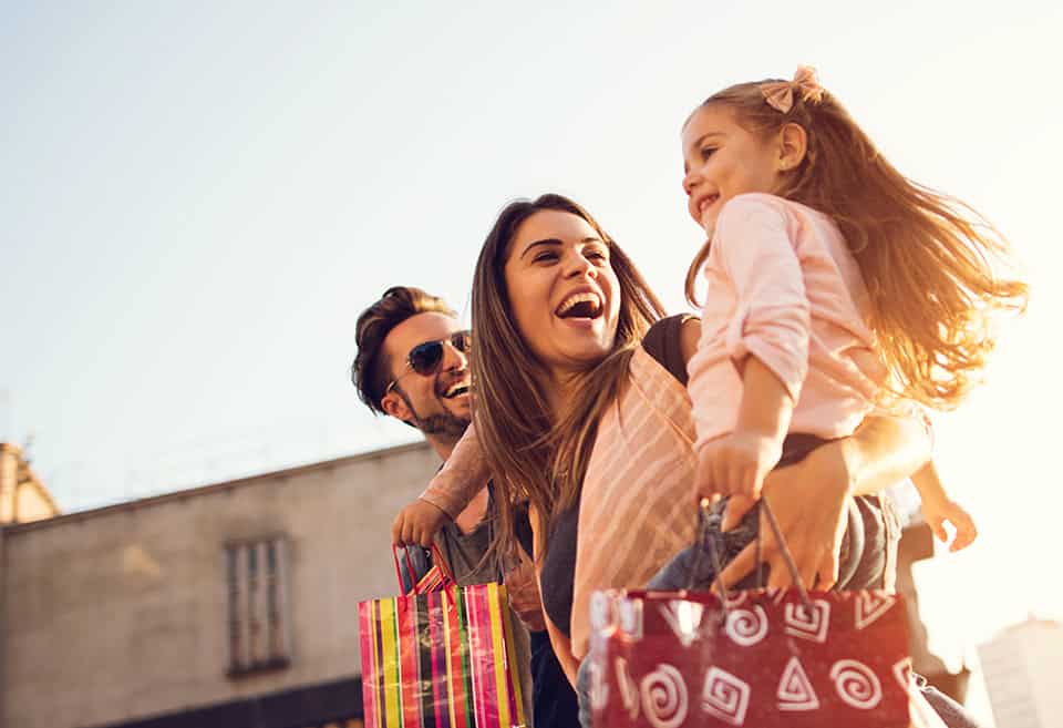 Young parents laugh and look at their child while holding shopping bags