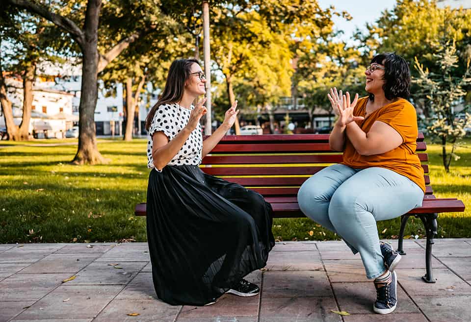 Two deaf people speak in sign language on a bench