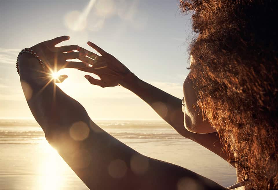 A person looking out at the sunset over the ocean and holding their hands out to block the sunlight
