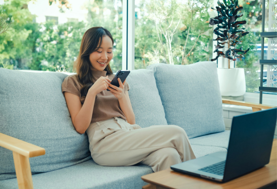 Young asian woman looking down at her phone, browsing BluPeak's FlexPay.