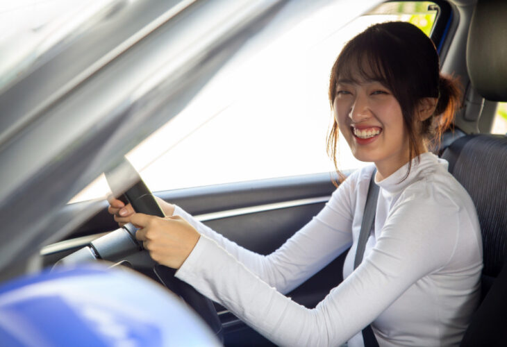 Young East/South Asian college student driving her car, smiling at the camera