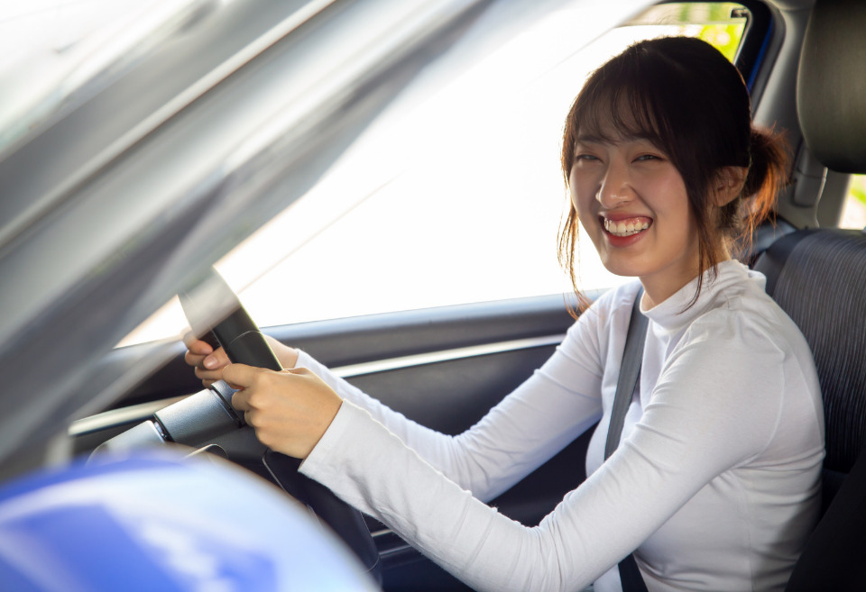 Young East/South Asian college student driving her car, smiling at the camera