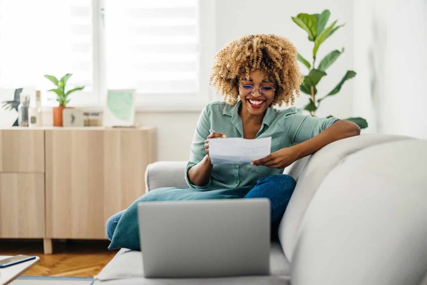 Black woman looking at document while working on her laptop so she can set up direct deposit and get an early payday.