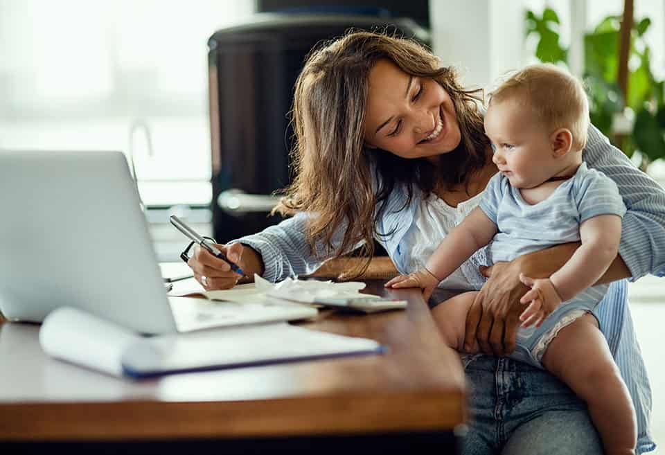 Smiling parent holding baby at table while working.