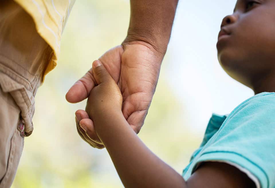 Small Black child holding hands with their parent.