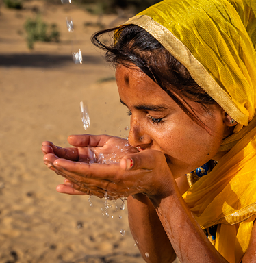 Girl with yellow head scarf drinking water with hands