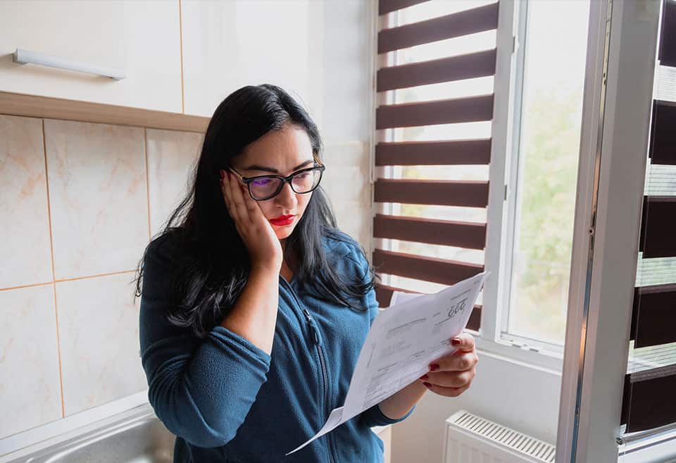 A person standing and looking concerned as they read over a financial document.