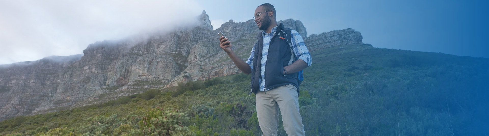 Man checking his phone, smiling on mountain