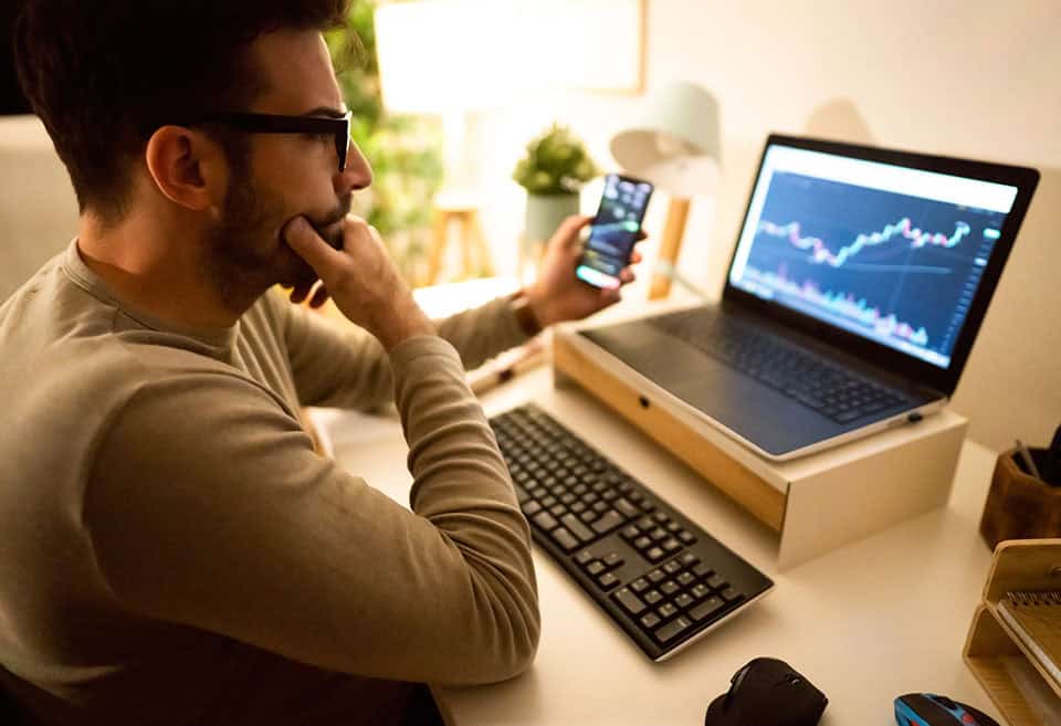 Person analyzing their investment portfolio on laptop and phone