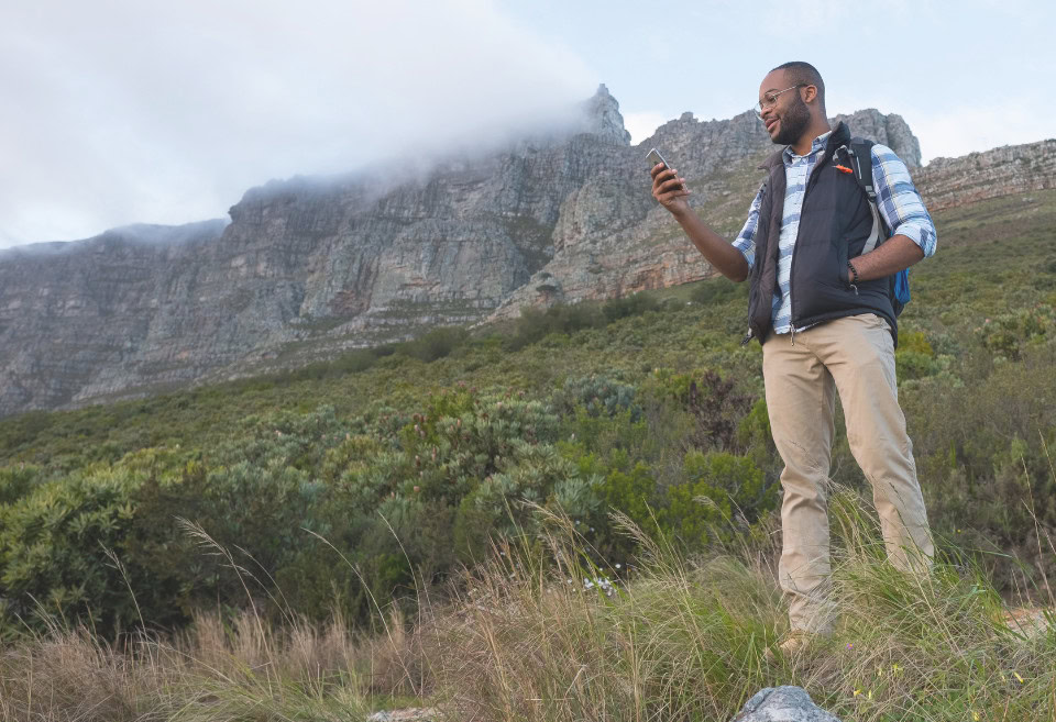 Man checking phone on mountain, smiling