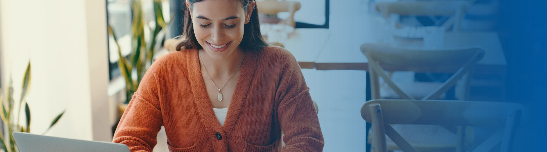 Woman in cafe smiling, looking down at her phone to browse BluPeak's new digital banking features