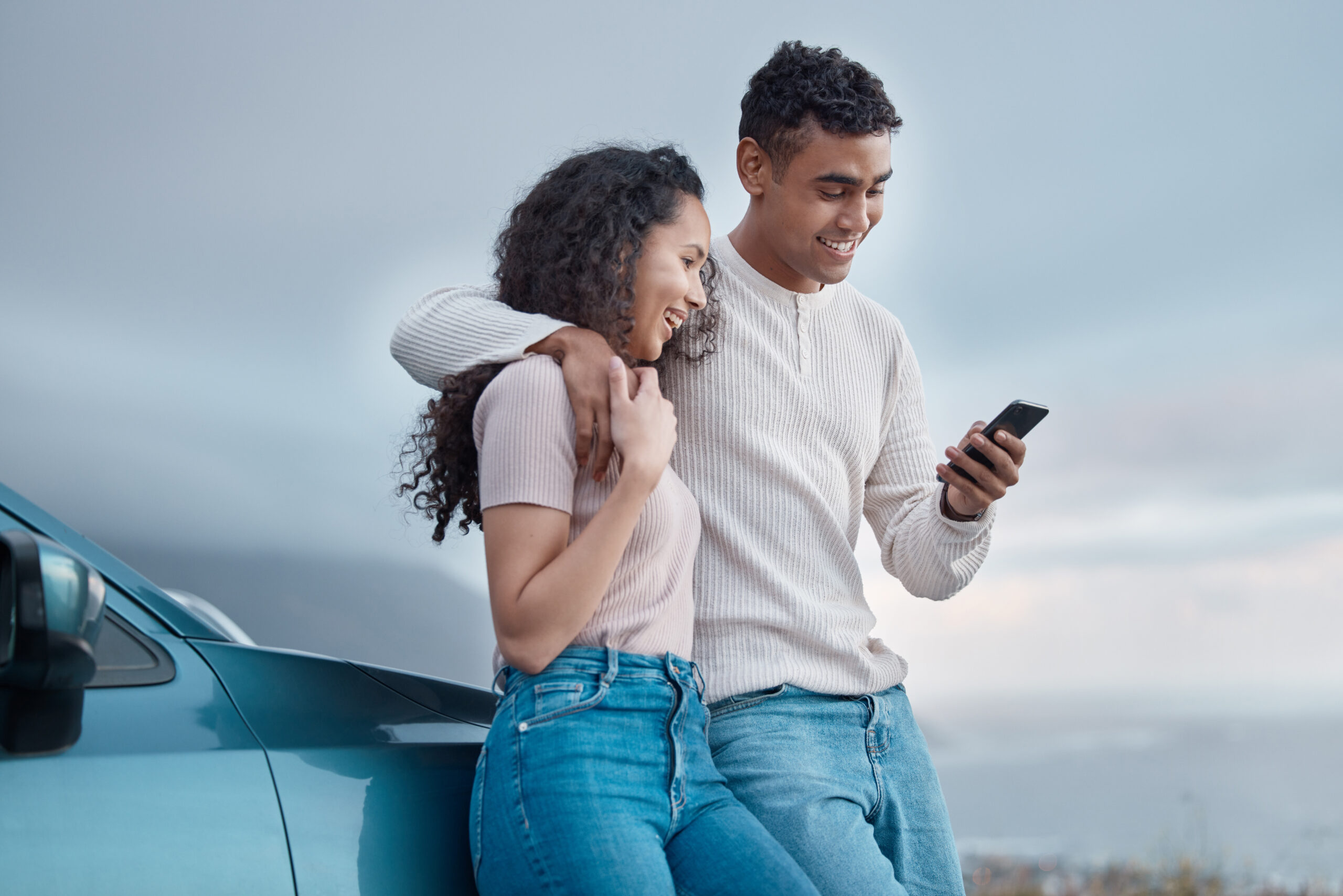 Couple standing next to car on smart phone