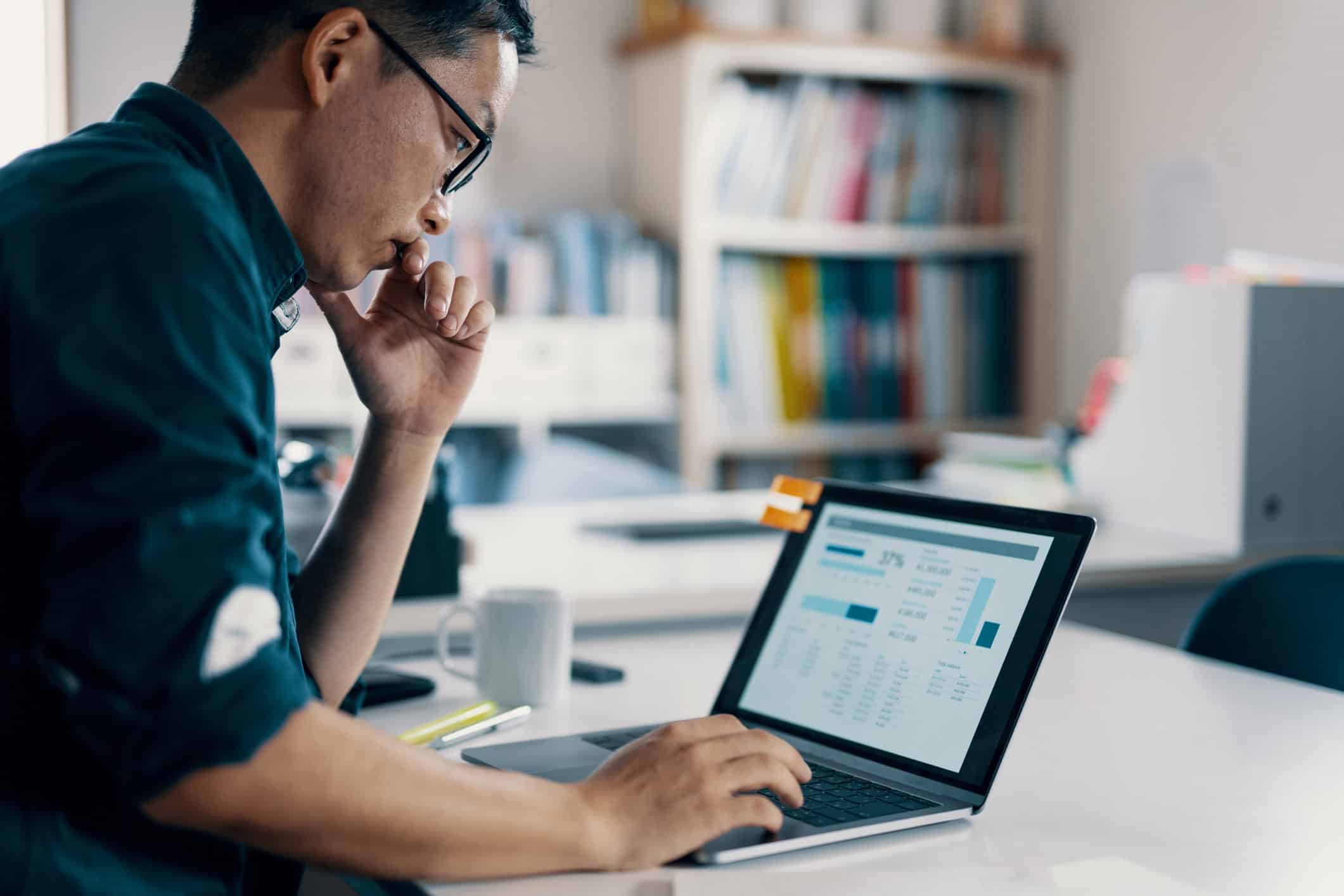 Man sitting at desk, looking at laptop.]