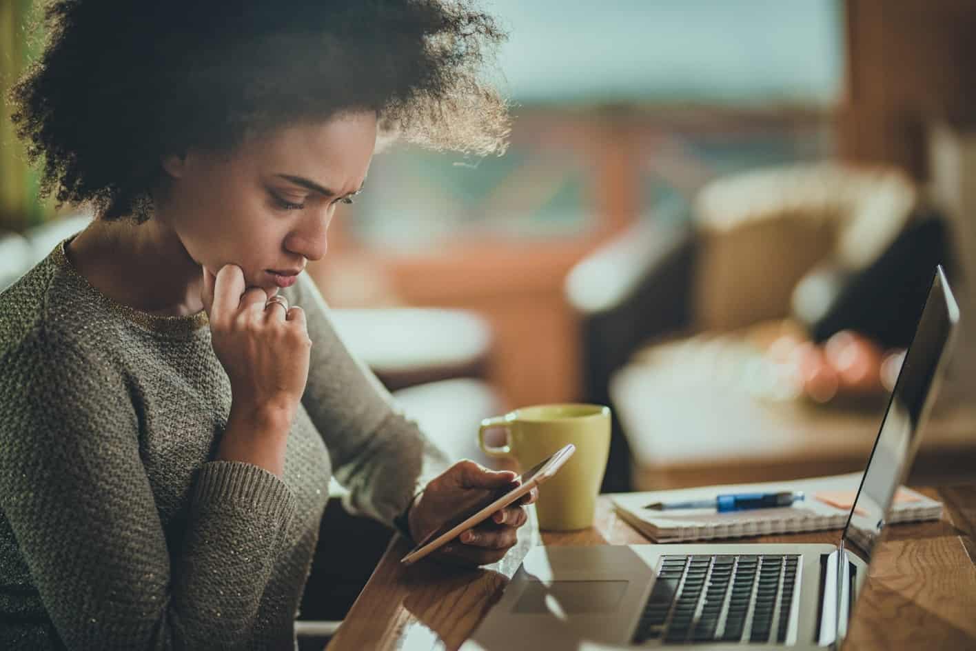 Black woman looks concerned using her cell phone after receiving an account alert.